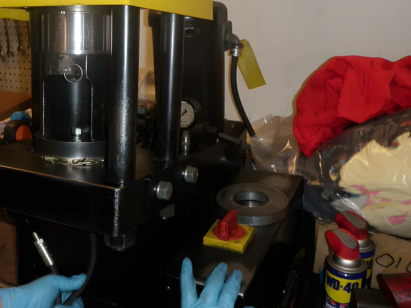 Technician crimping a hydraulic hose fitting on a bench crimper